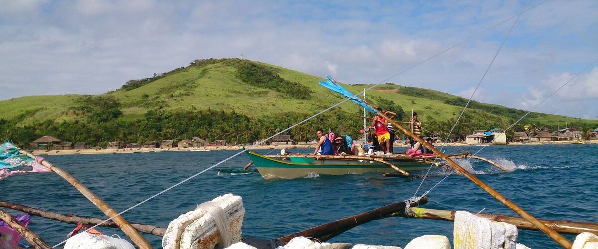 A boat on calm waters with a green hill in the background.