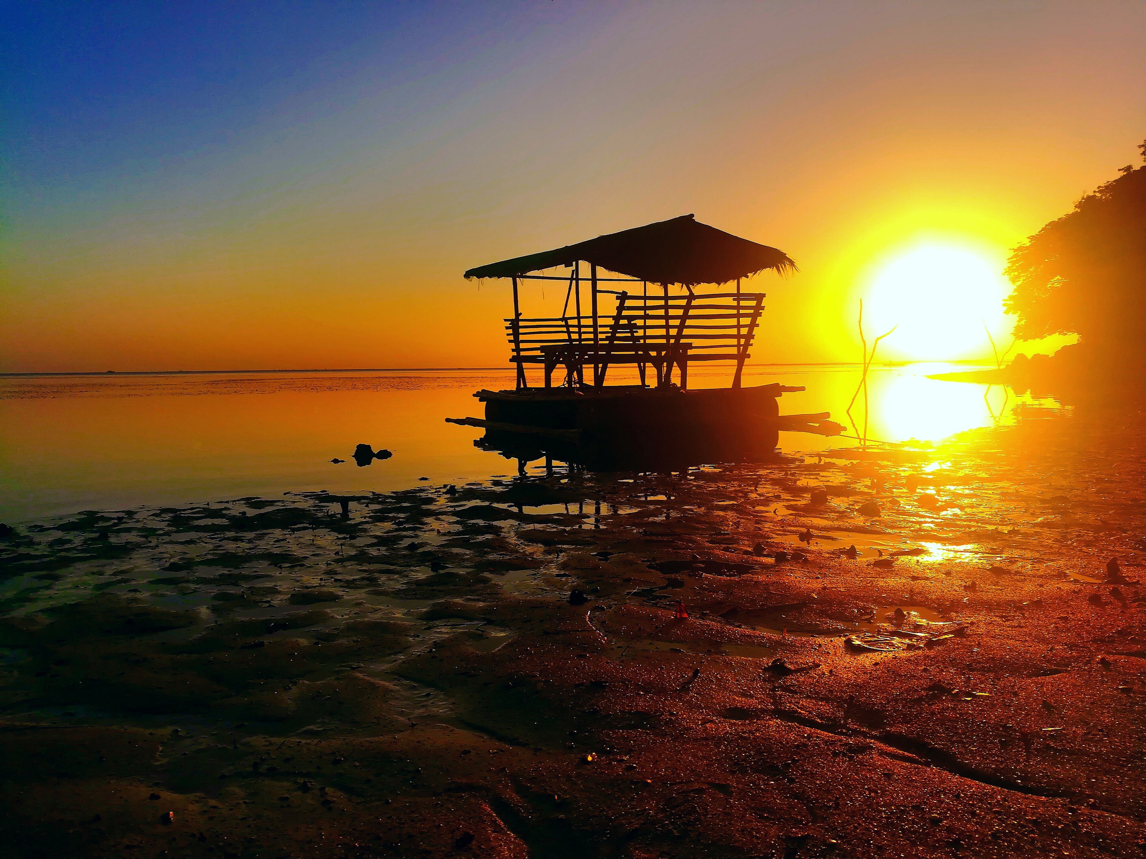 A wooden structure on stilts by a calm body of water during sunset.