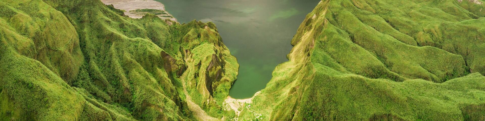 A green valley with a lake surrounded by mountains.