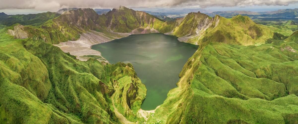 A green valley with a lake surrounded by mountains.
