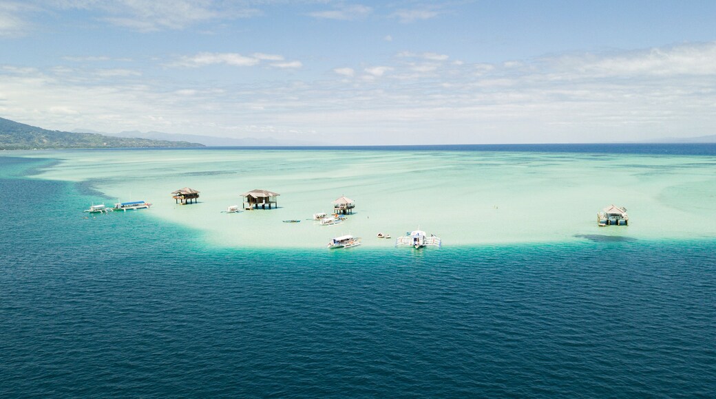 A tropical island with clear turquoise waters, several overwater bungalows, and a few boats.
