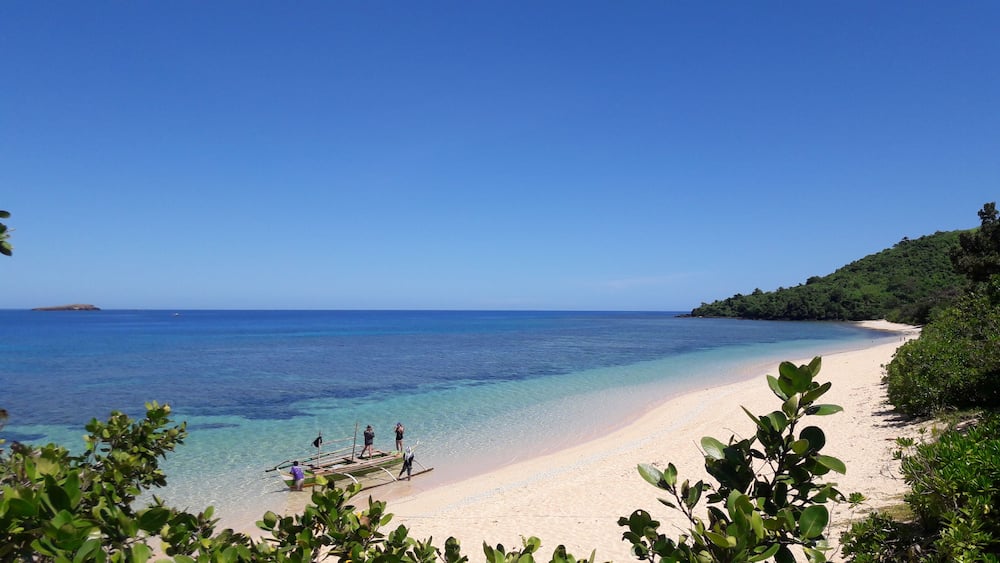 Une plage à l’eau turquoise et limpide, bordée d’un rivage sablonneux et d’une végétation luxuriante.