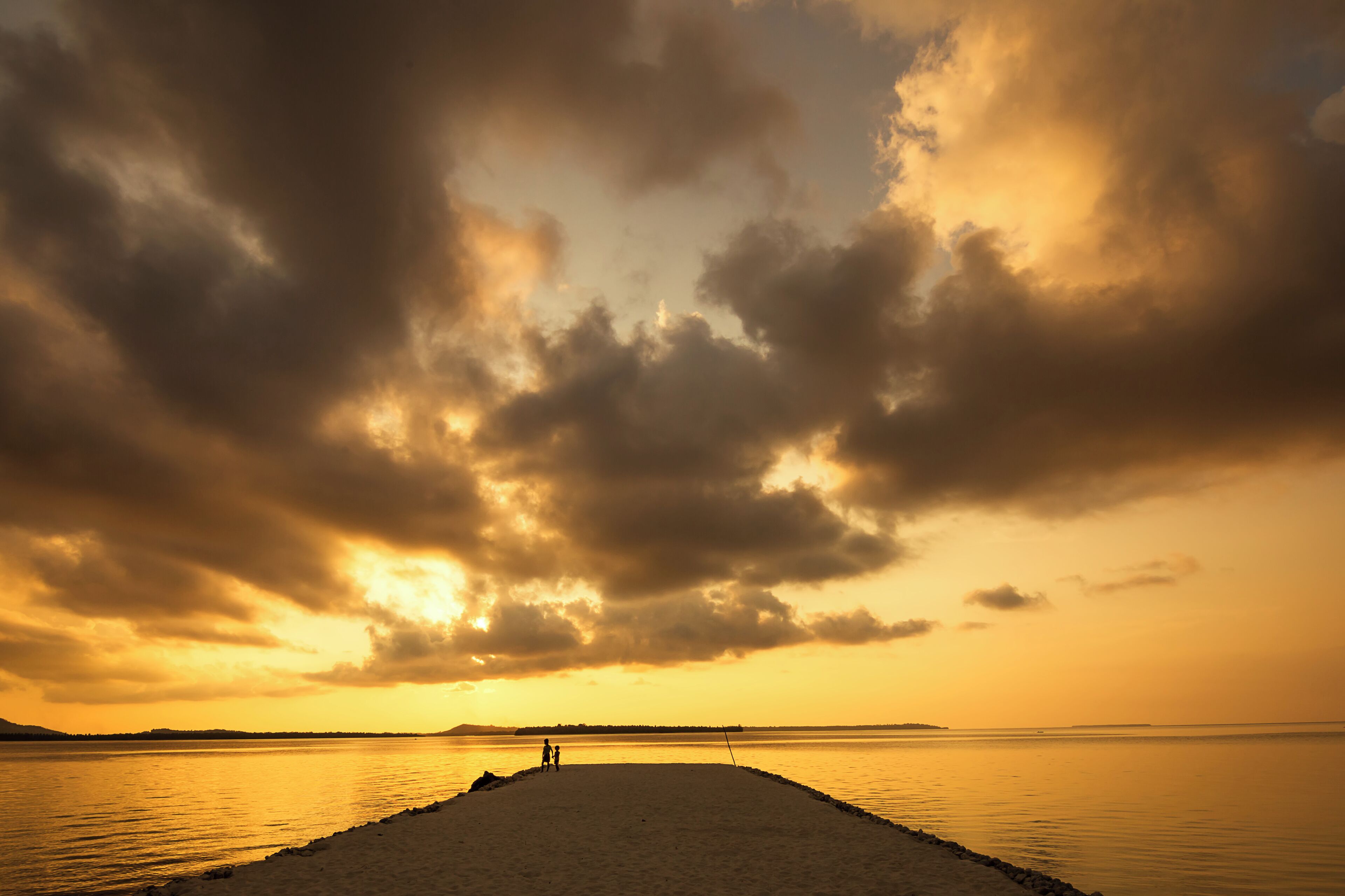 A boy and his younger sister stand at the edge of the island's wharf surrounded by the warm magnificent light of golden hour.