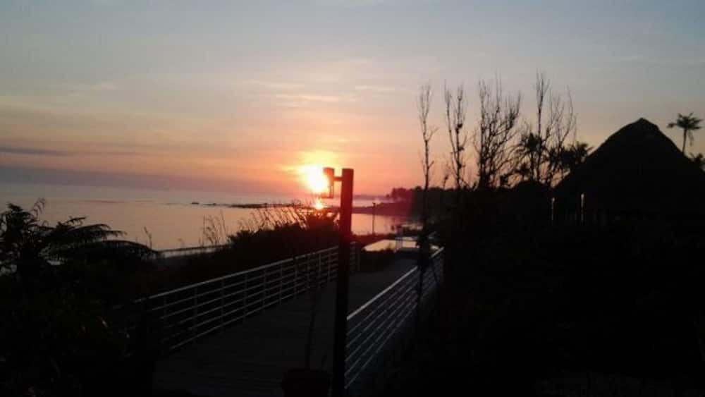 A sunset over a beach with a wooden walkway and a thatched-roof structure.