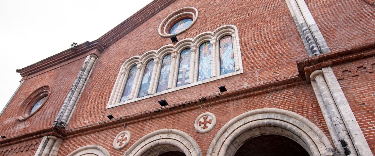 A red brick building with arched windows and a cross on the roof.