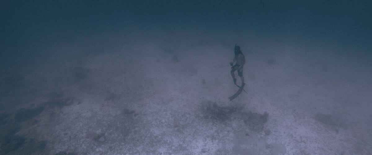 A diver underwater with a long snorkel and fins, surrounded by a sandy seabed.