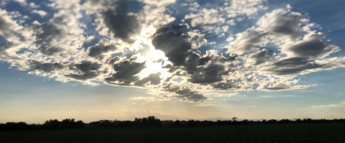 A field with scattered clouds and the sun shining through.
