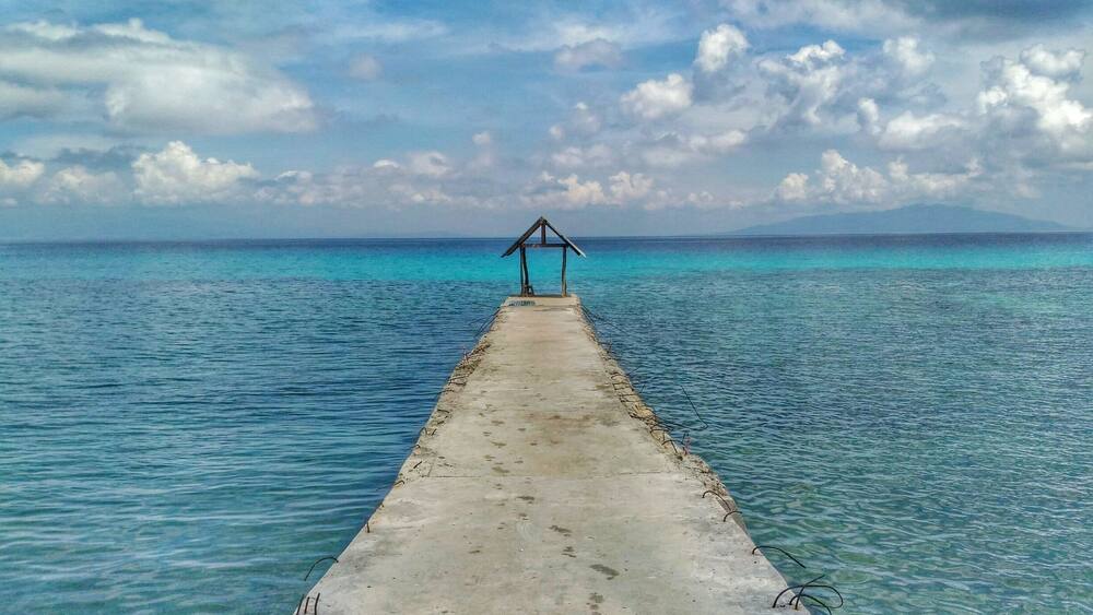 A concrete pier extending into turquoise waters with a wooden structure at the end.