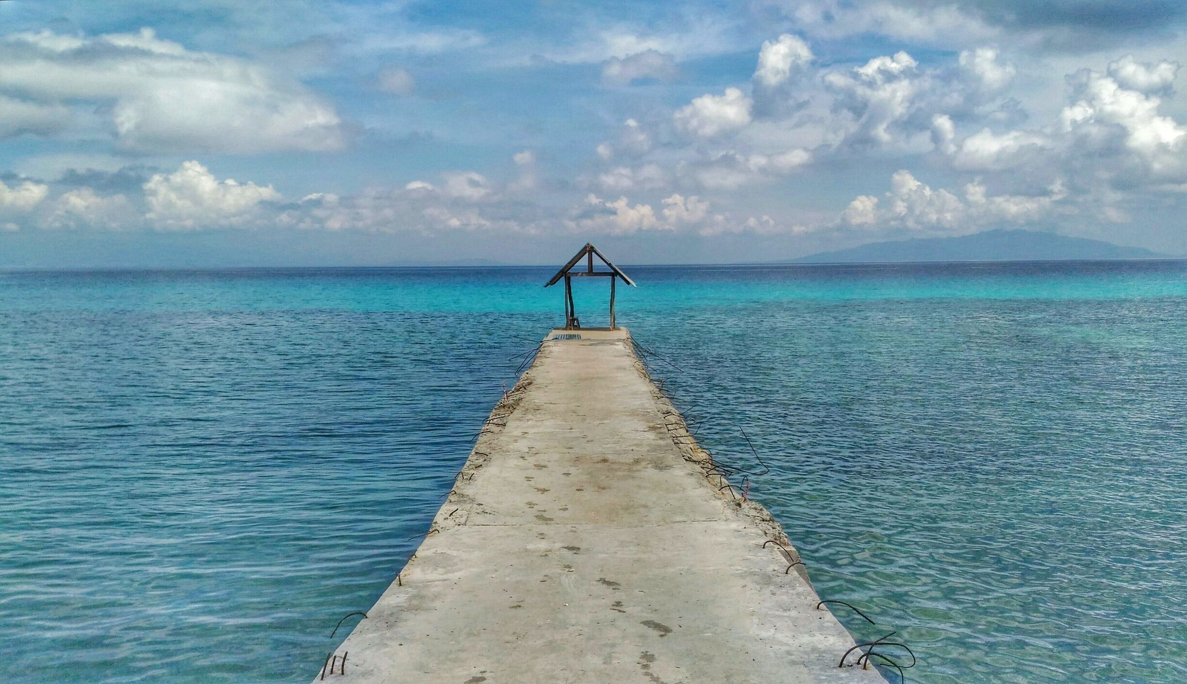 A concrete pier extending into turquoise waters with a wooden structure at the end.