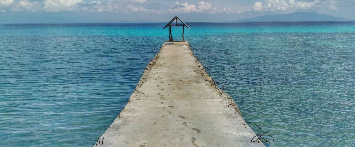 A concrete pier extending into turquoise waters with a wooden structure at the end.