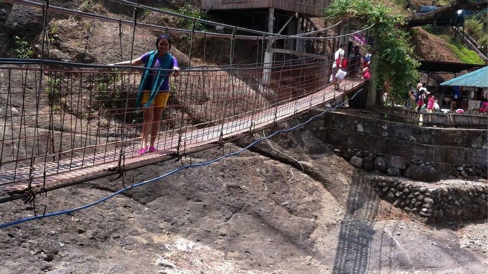 A rope bridge over a rocky terrain with a wooden structure in the background.