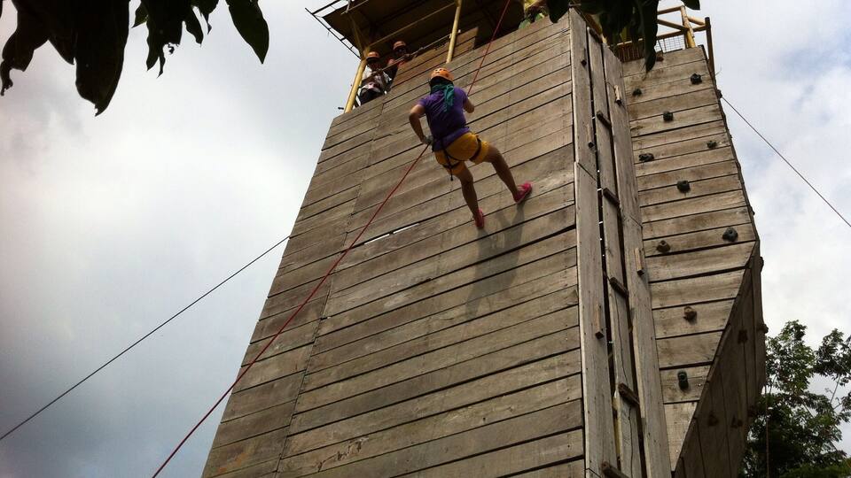 A person climbing a wooden tower with ropes.