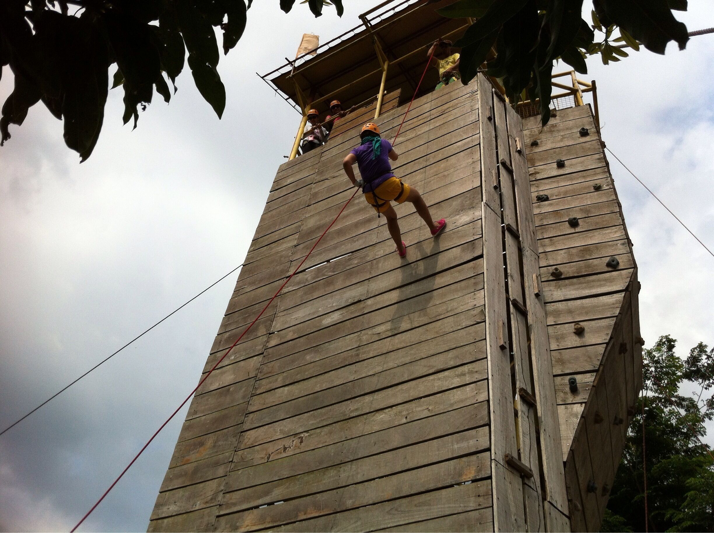 A person climbing a wooden tower with ropes.