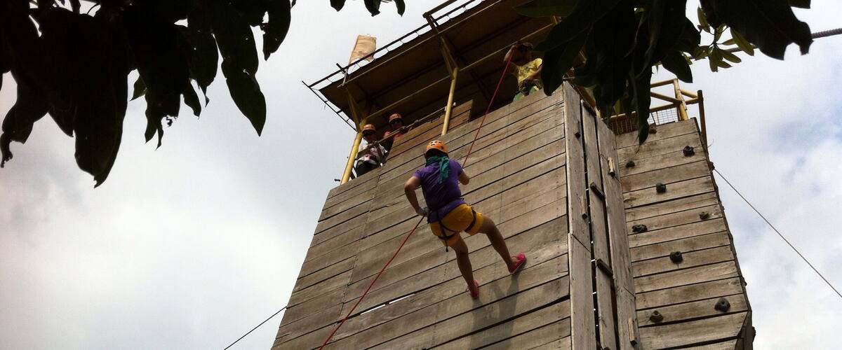 A person climbing a wooden tower with ropes.