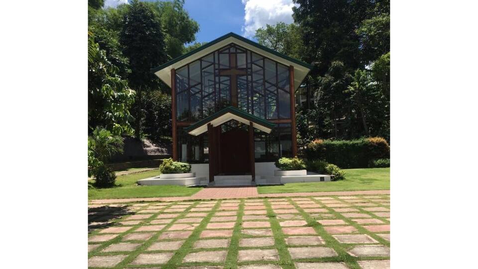 A modern house with a glass facade, surrounded by a well-manicured lawn and trees.