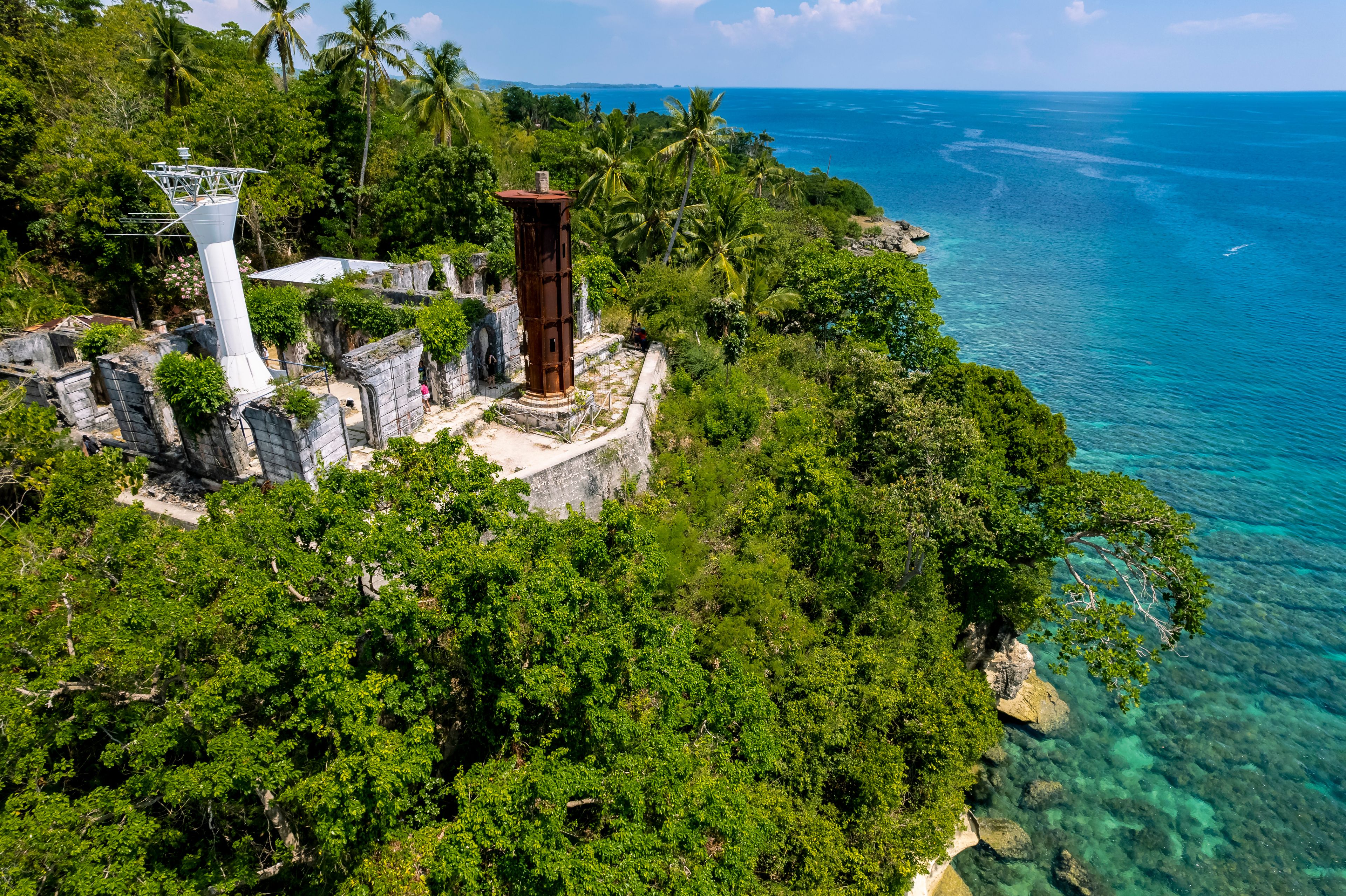 A coastal landscape with lush greenery, a lighthouse, and clear blue waters.