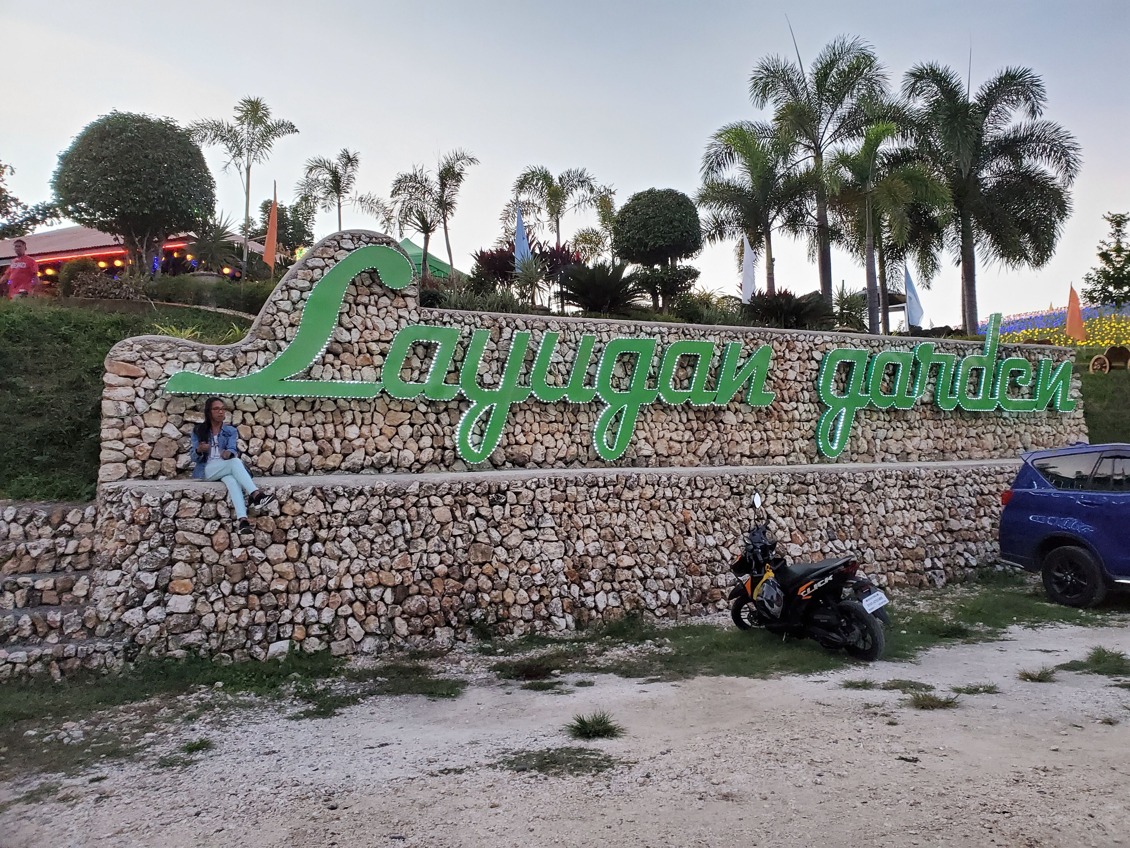 A stone wall with the sign 'Lajuggan garden' and a person sitting on a bench.