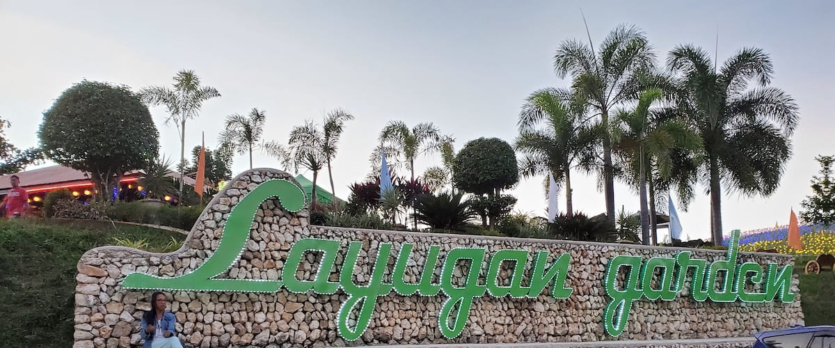 A stone wall with the sign 'Lajuggan garden' and a person sitting on a bench.