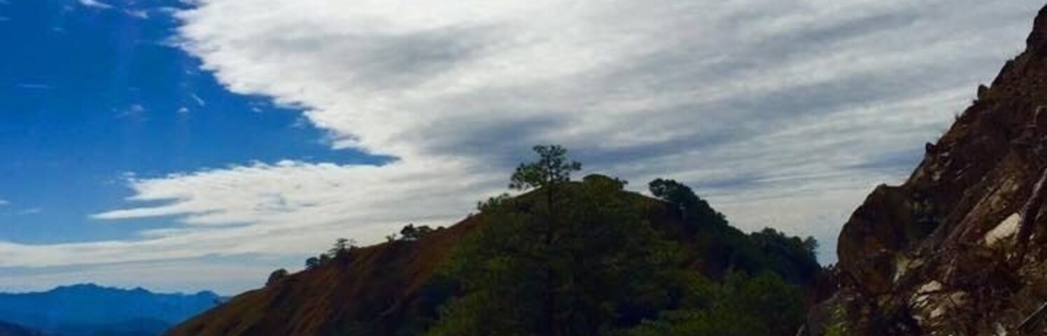 Una carretera sinuosa en la montaña con cielo azul despejado y nubes dispersas.