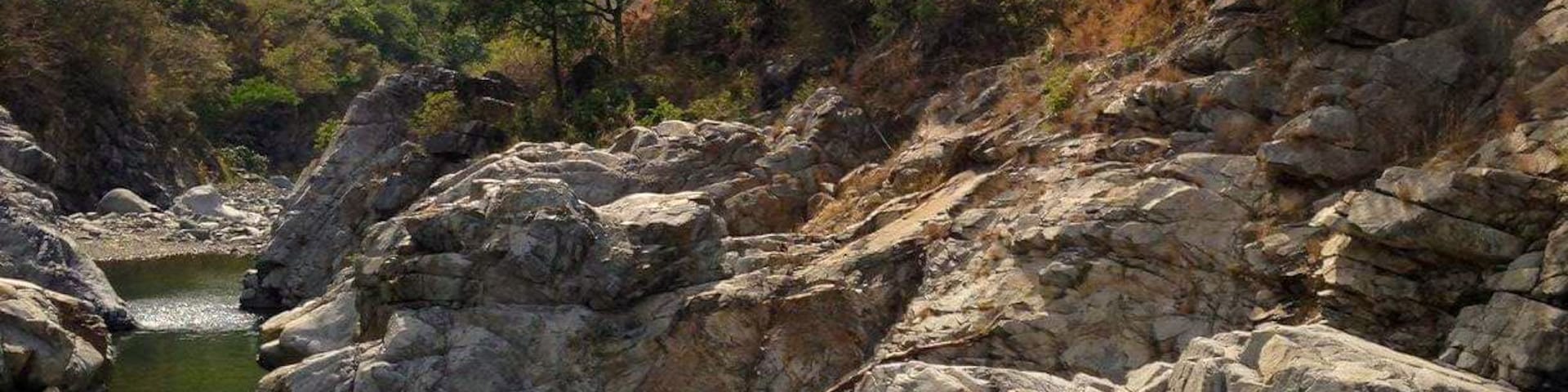 A rocky riverbed with a small stream, surrounded by hills and trees.