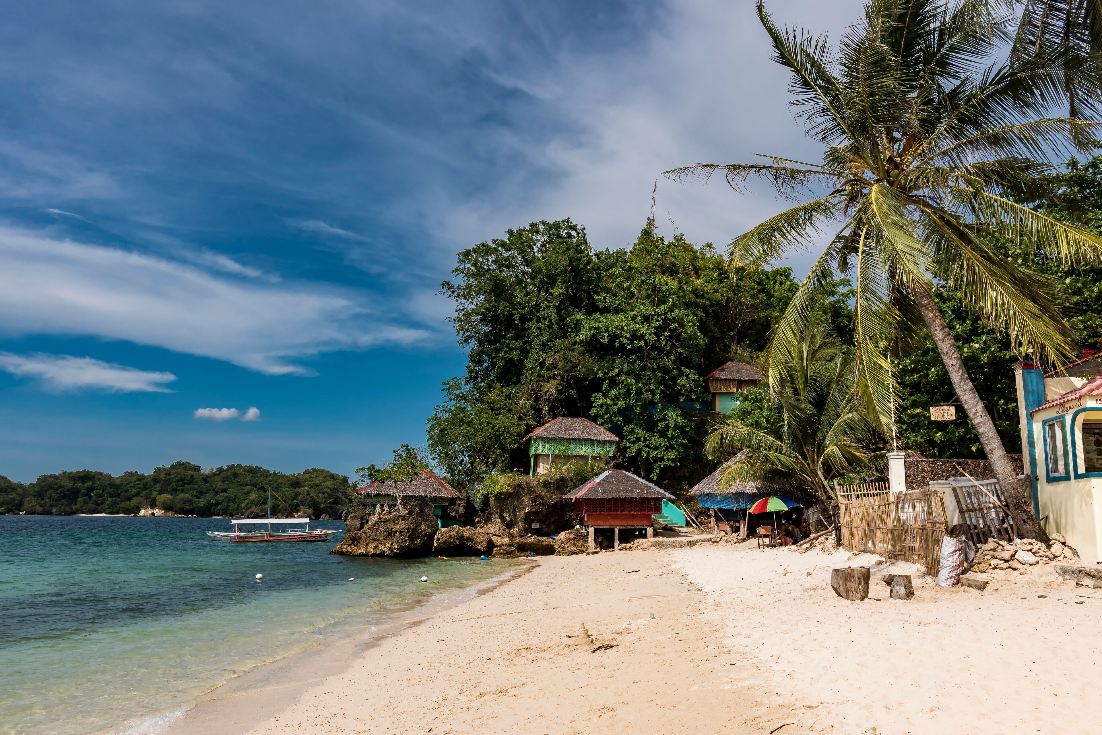 A beach with clear water, palm trees, and thatched-roof huts.