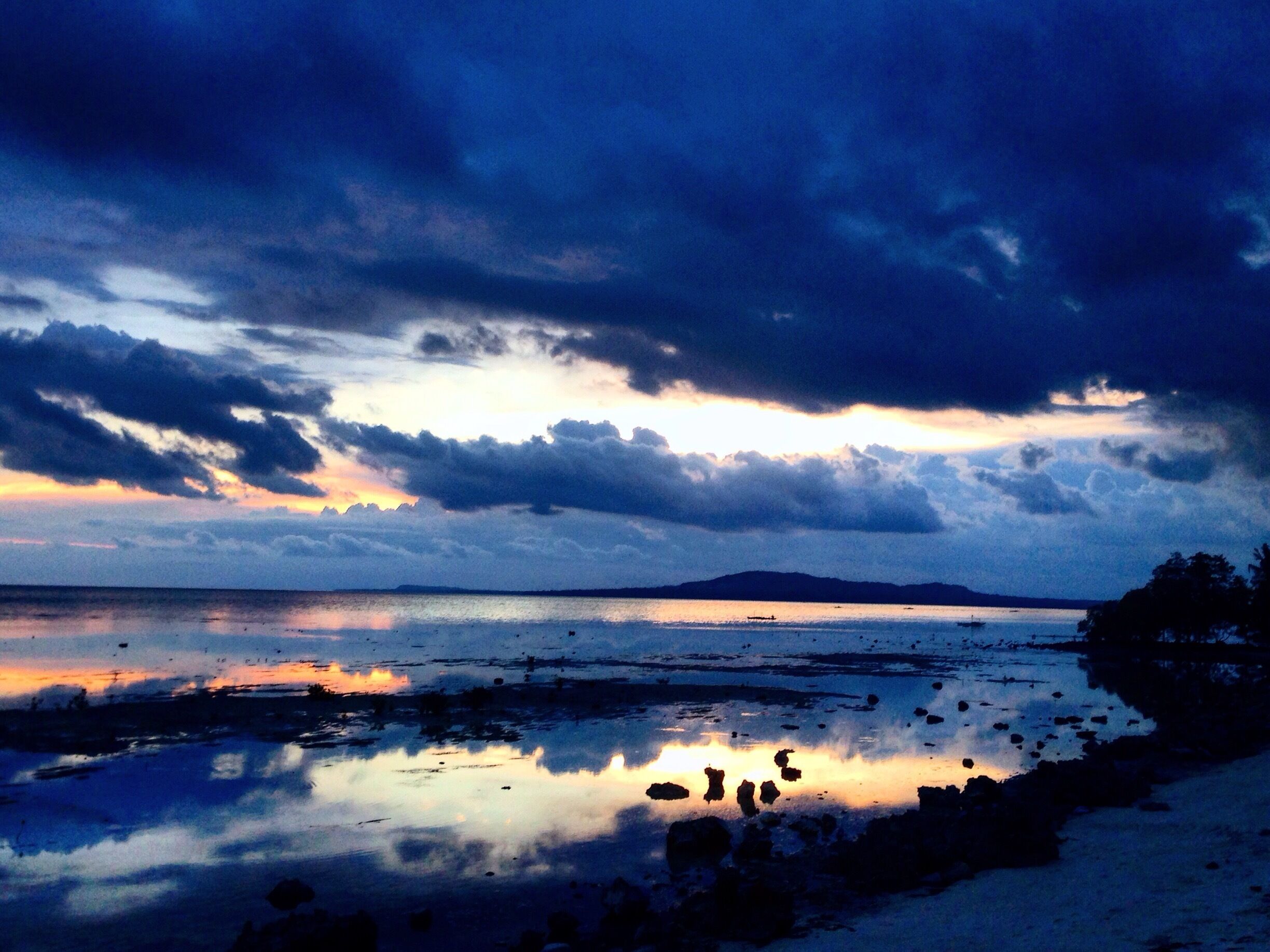 A coastal landscape with a sunset, calm sea, and rocky shoreline.