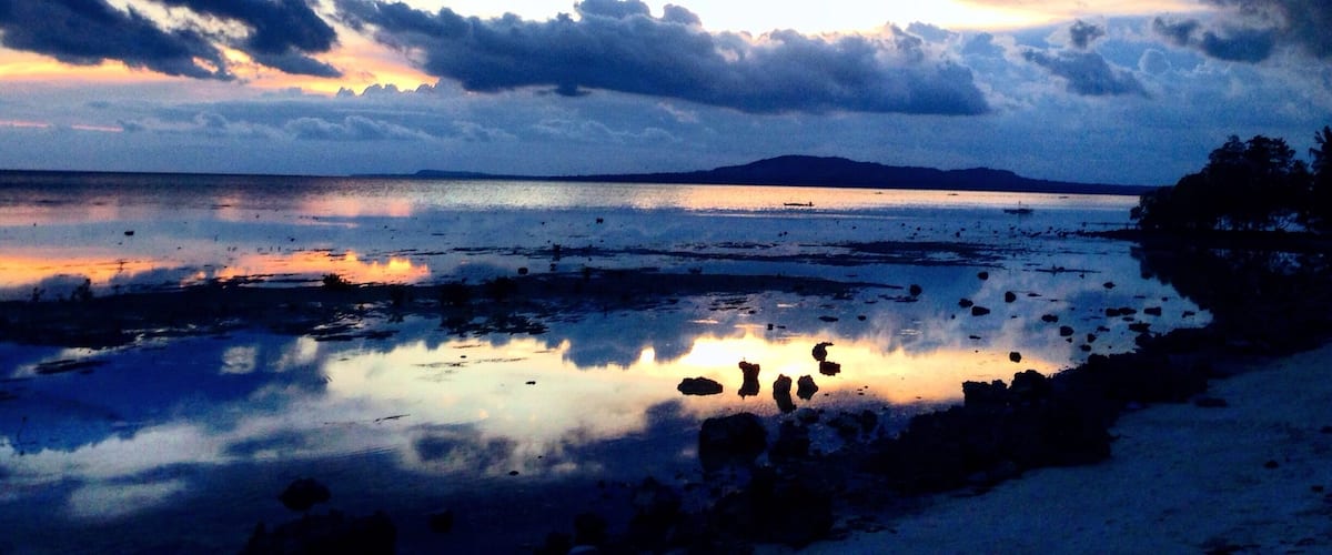 A coastal landscape with a sunset, calm sea, and rocky shoreline.
