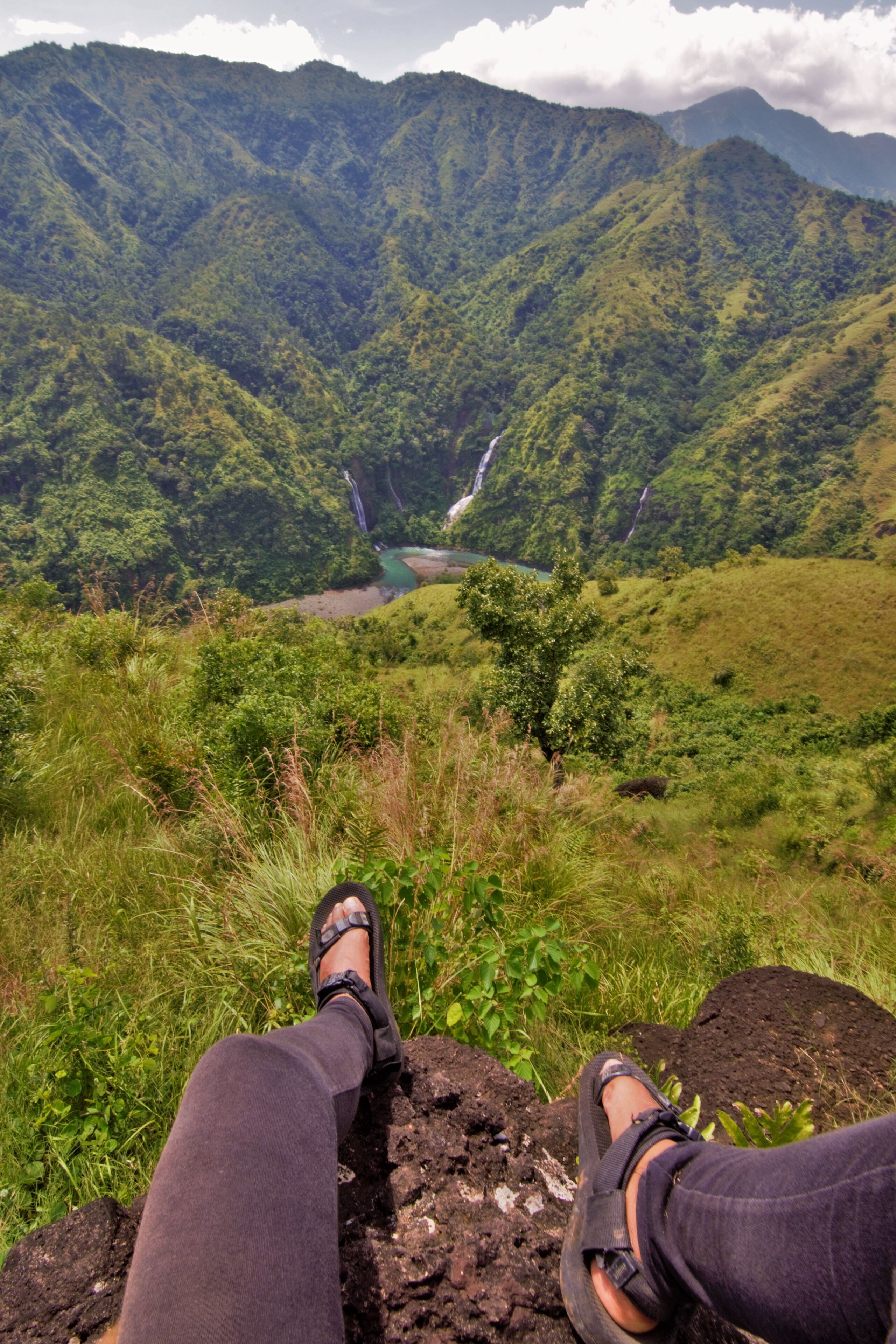 A person sitting on a rock overlooking a lush valley with waterfalls.
