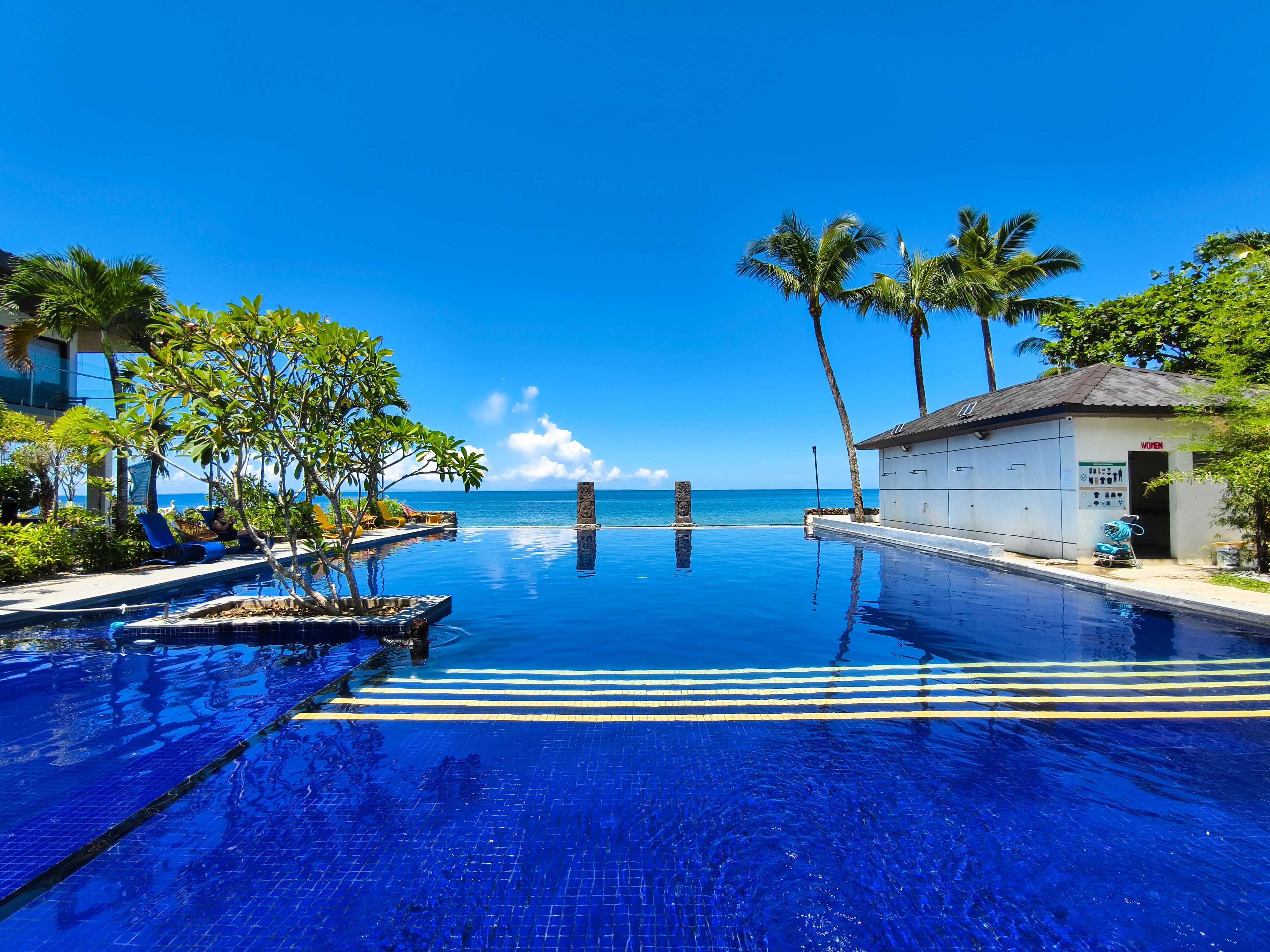 A clear blue infinity pool with palm trees and a view of the ocean.