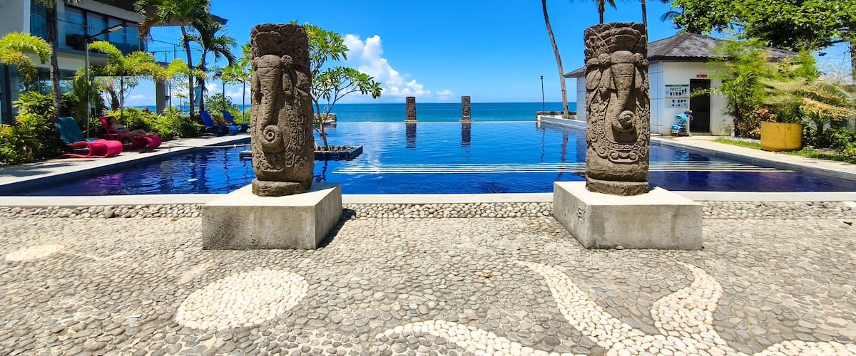 A pool with two stone sculptures, a clear blue sky, and a view of the ocean.