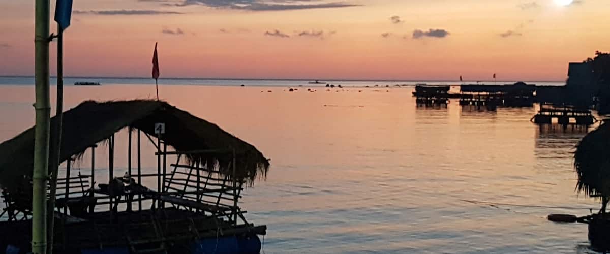 A calm sea at sunset with boats and a thatched structure.