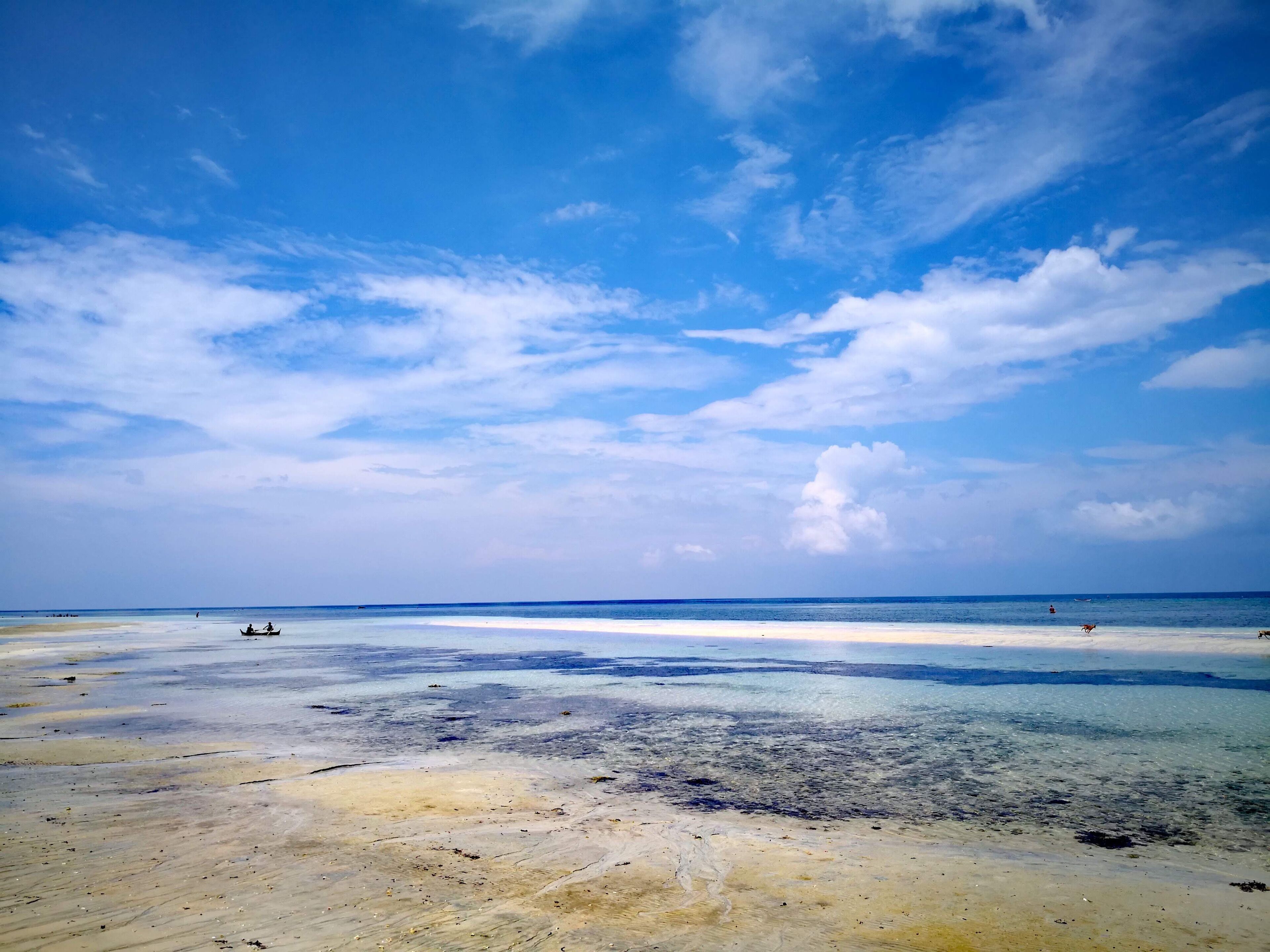 A beach with clear blue water and a sandy shore under a partly cloudy sky.