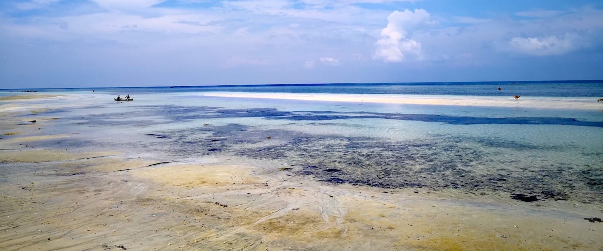 A beach with clear blue water and a sandy shore under a partly cloudy sky.