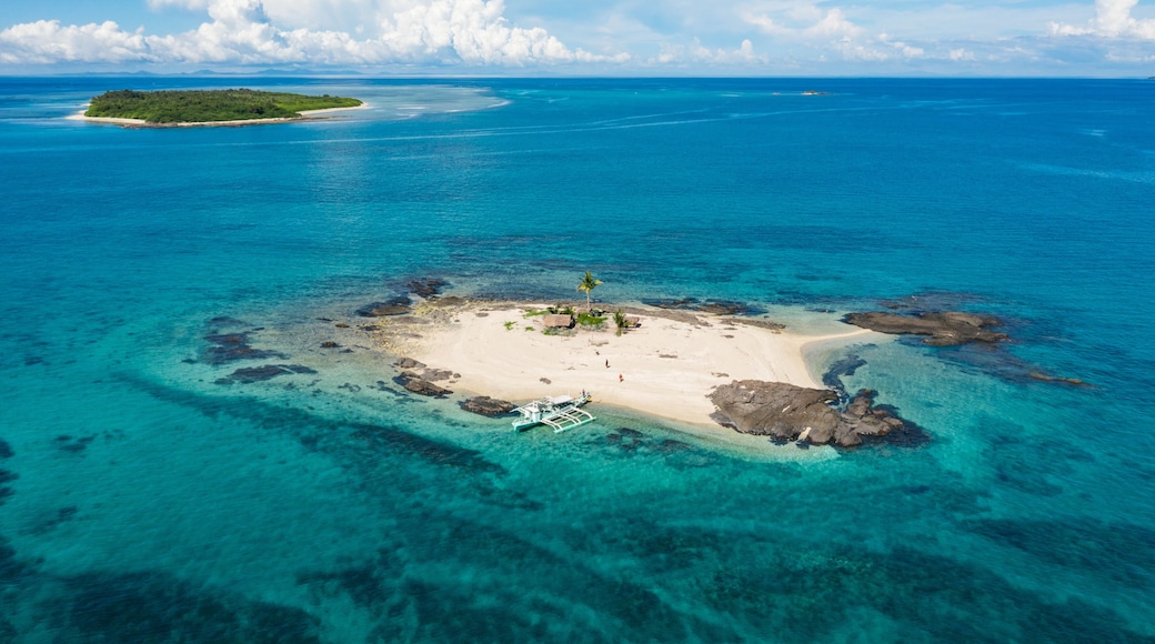 Aerial view of a small sandy island surrounded by turquoise waters, with rocky outcrops and distant lush island, Bancal, Western Visayas, Philippines.