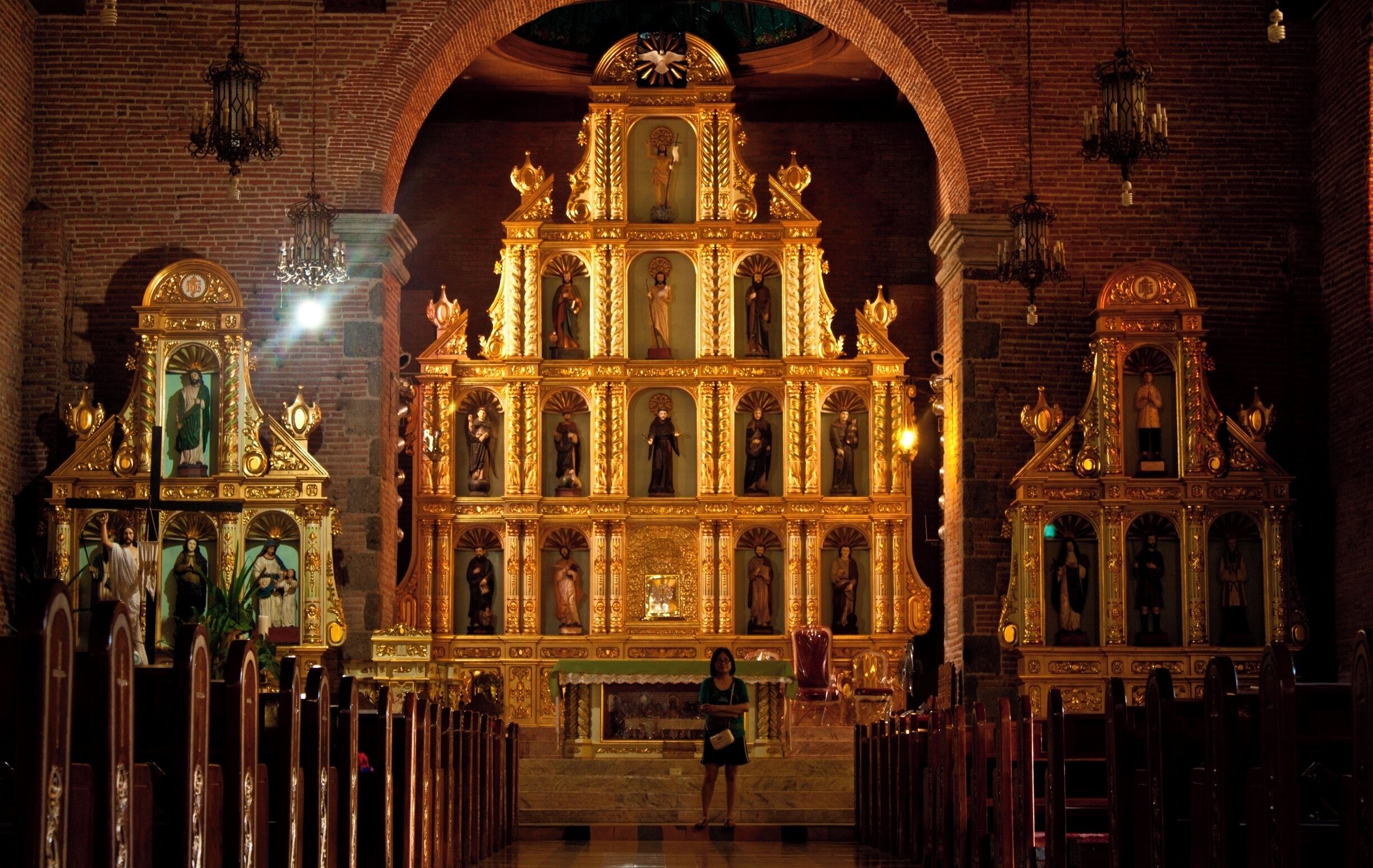 An ornate church interior with a central altar, statues, and a woman standing in the foreground.