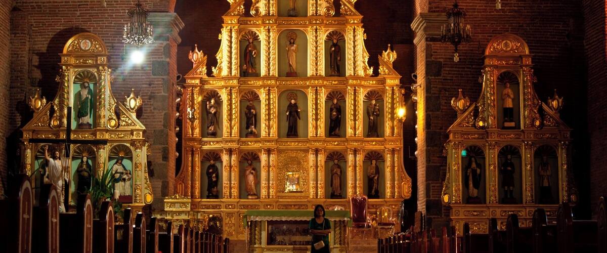 An ornate church interior with a central altar, statues, and a woman standing in the foreground.