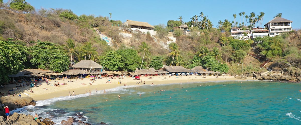 A beach with clear turquoise waters, rocky shoreline, and thatched-roof huts.