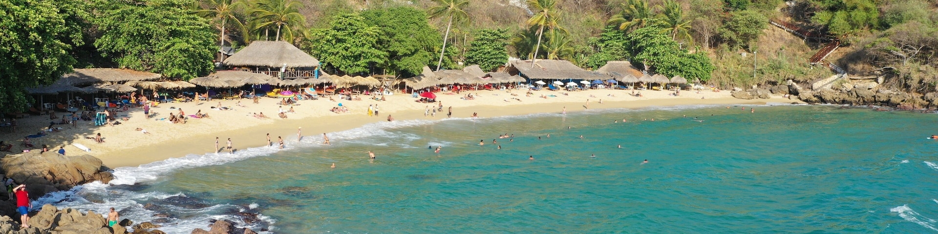 A beach with clear turquoise waters, rocky shoreline, and thatched-roof huts.