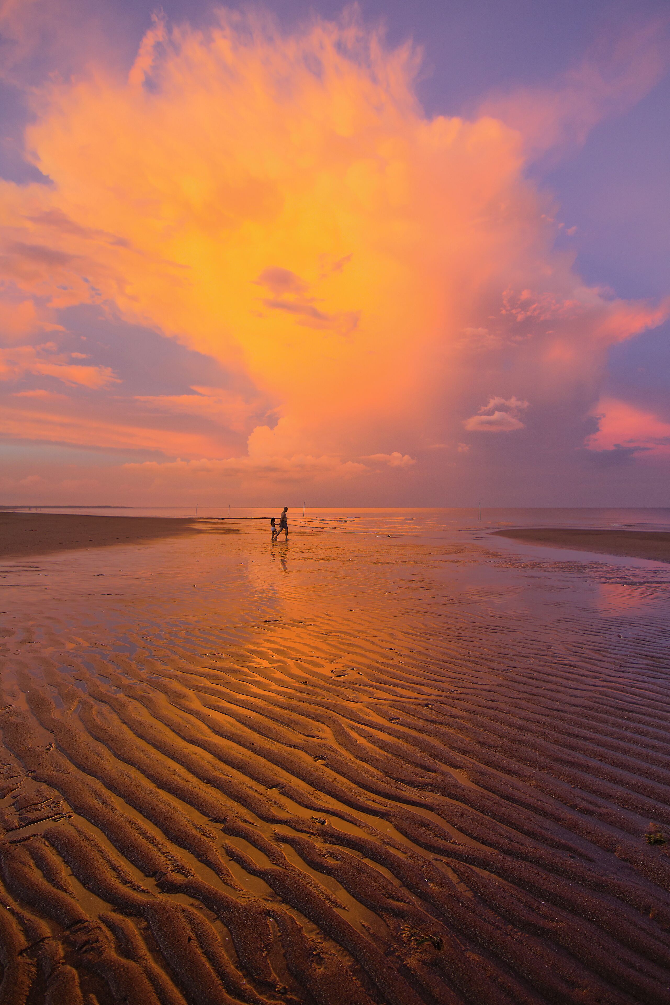 The vibrant colors of the sunset paint the quiet beaches of San Juan in Batangas, Philippines while two silhouettes take a nice evening stroll by the sea.