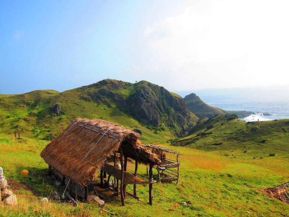 A thatched-roof hut on a grassy hillside overlooking a coastal landscape.