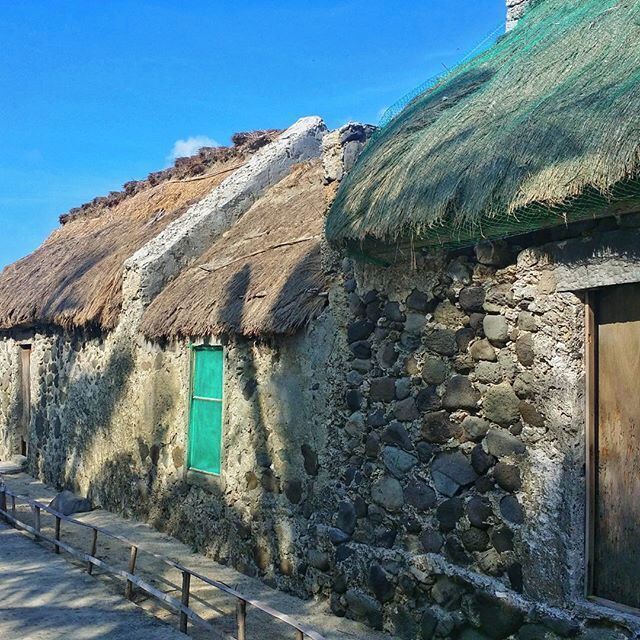 A stone house with a thatched roof and a green window.