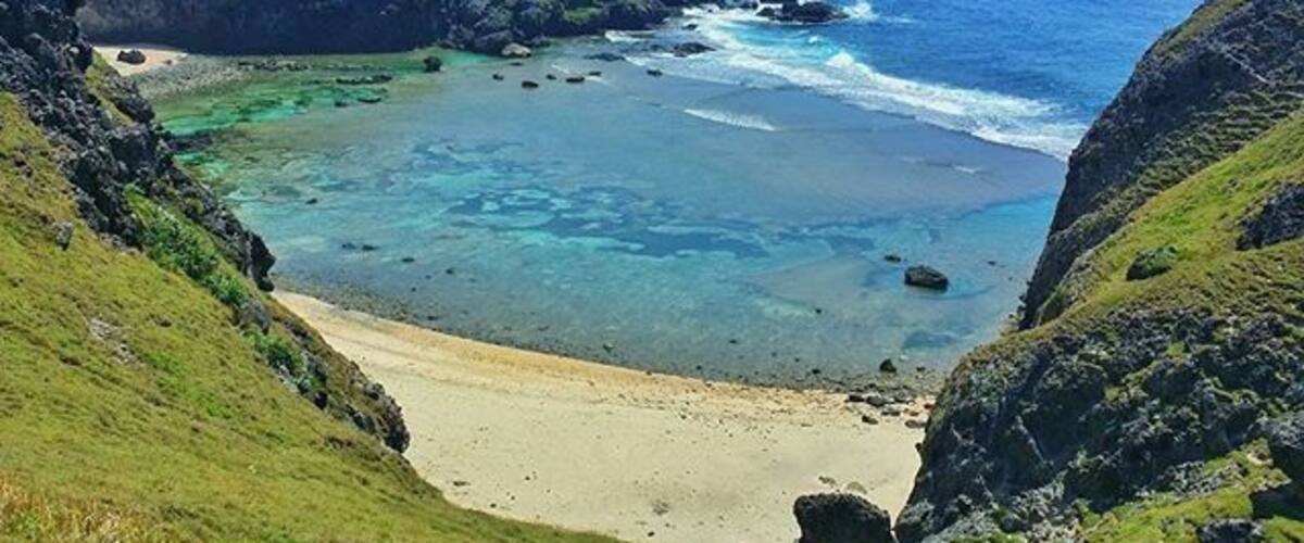 Un paysage côtier avec une mer bleue et limpide, une plage de sable et des collines verdoyantes.