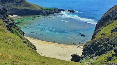 Un paisaje costero con mar azul cristalino, una playa arenosa y colinas verdes.