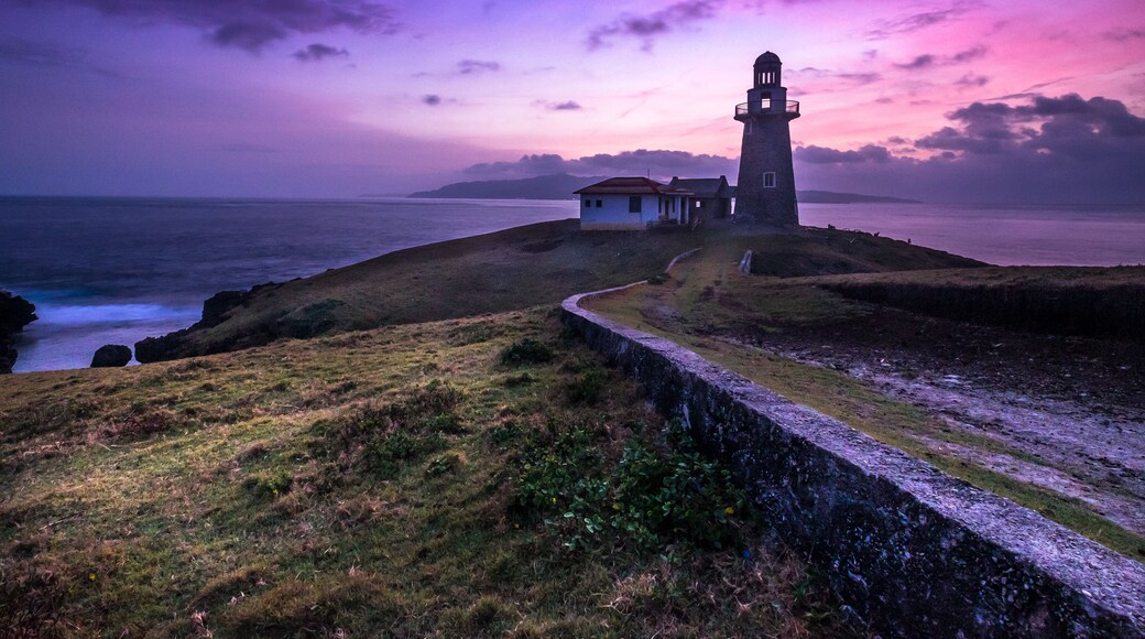 Een vuurtoren op een heuvel vol gras met uitzicht op de oceaan bij zonsondergang.