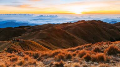 A mountainous landscape with rolling hills and a sunset in the background.