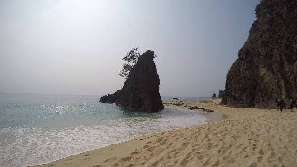 Ein Sandstrand mit großen Felsformationen und ruhigem Wasser.