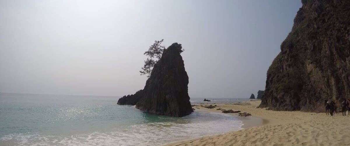 A sandy beach with large rock formations and calm waters.