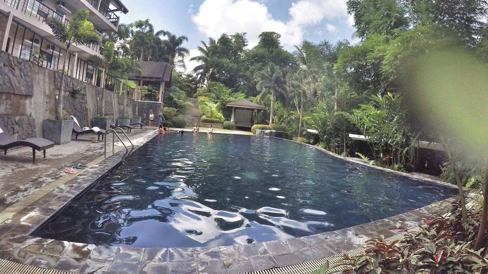 A swimming pool with lounge chairs, surrounded by tropical vegetation and a stone wall.