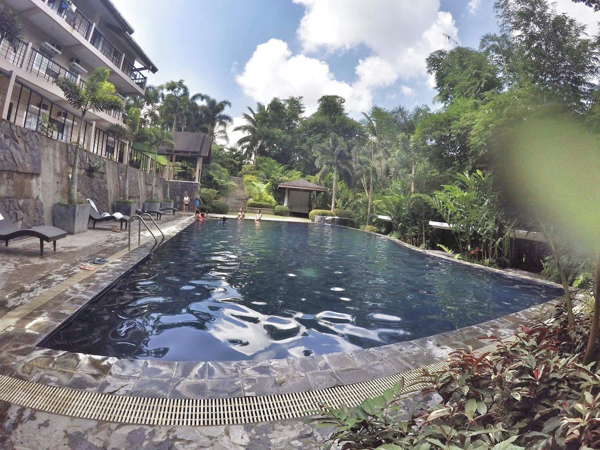 A swimming pool with lounge chairs, surrounded by tropical vegetation and a stone wall.