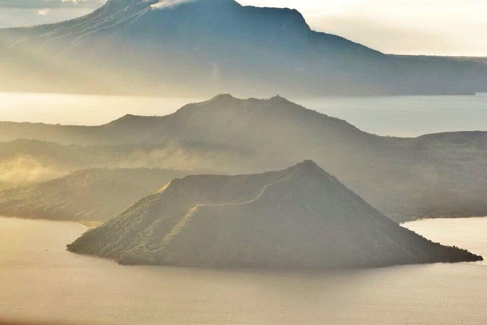 Un paysage montagneux dominé par un volcan imposant et bordé d’une étendue d’eau calme.